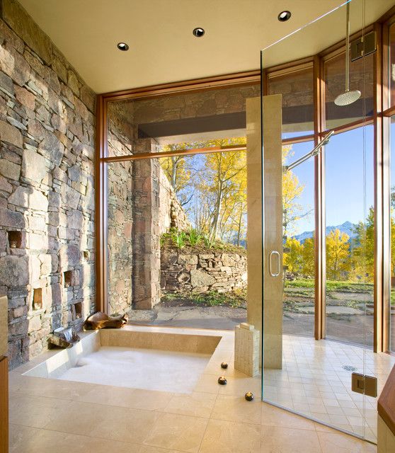 a large bathroom with stone walls and floor to ceiling glass doors that open up into the outdoors