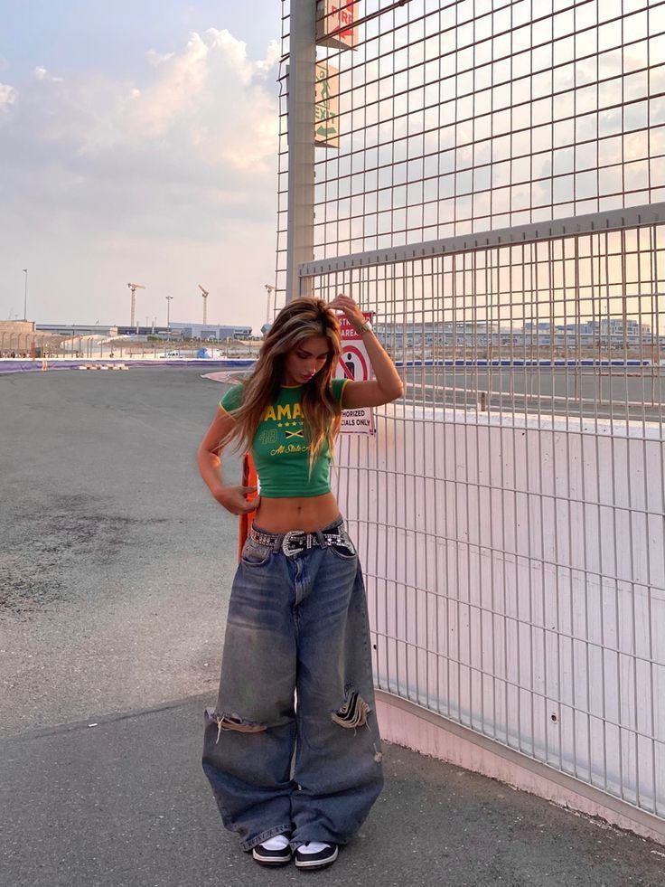 a woman standing in front of a fence with her hands on her head and wearing ripped jeans