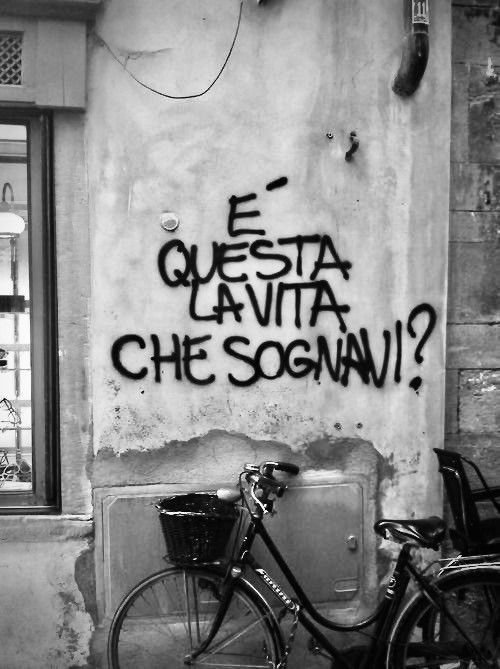 a bike parked next to a building with graffiti on it's side and the words, e ques ata la vita che sogni?