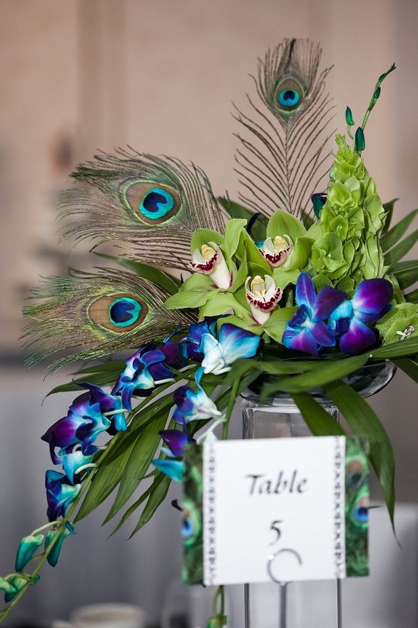 there is a vase with flowers and peacock feathers on the table at this wedding reception