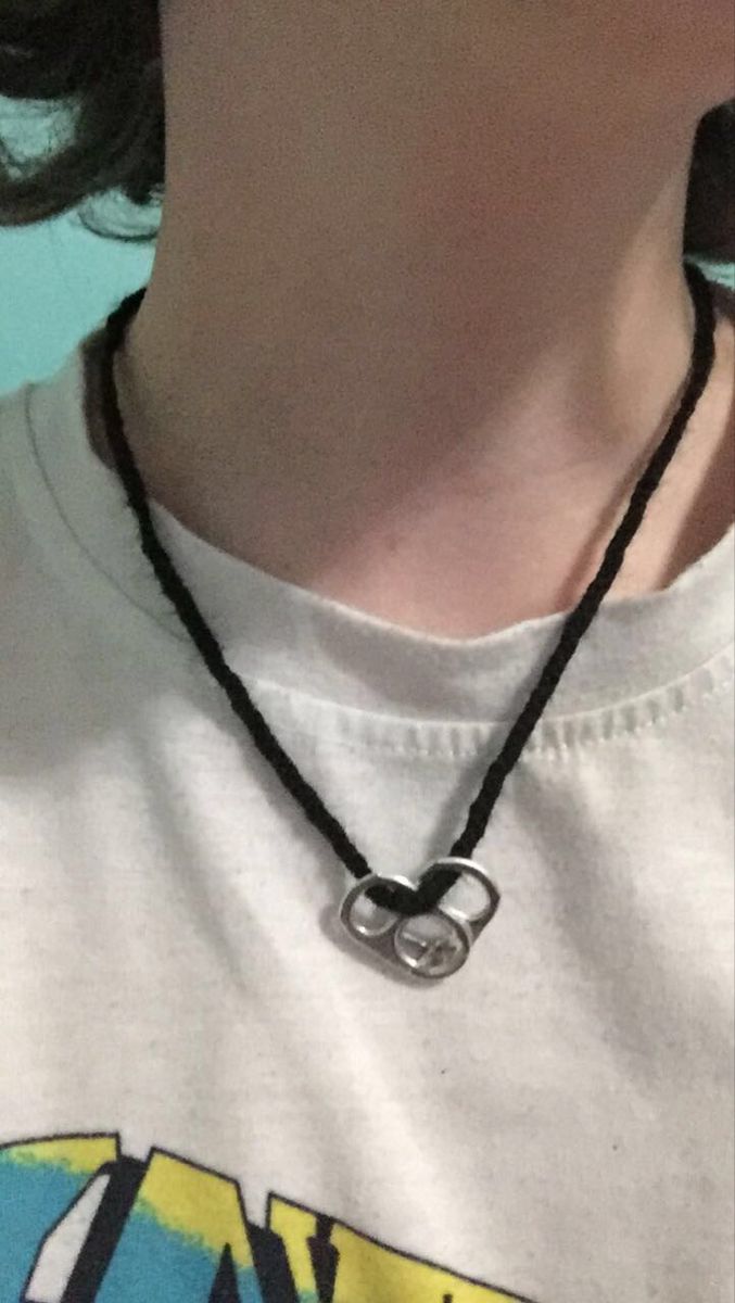 a close up of a person wearing a white shirt and black necklace with a silver ring on it