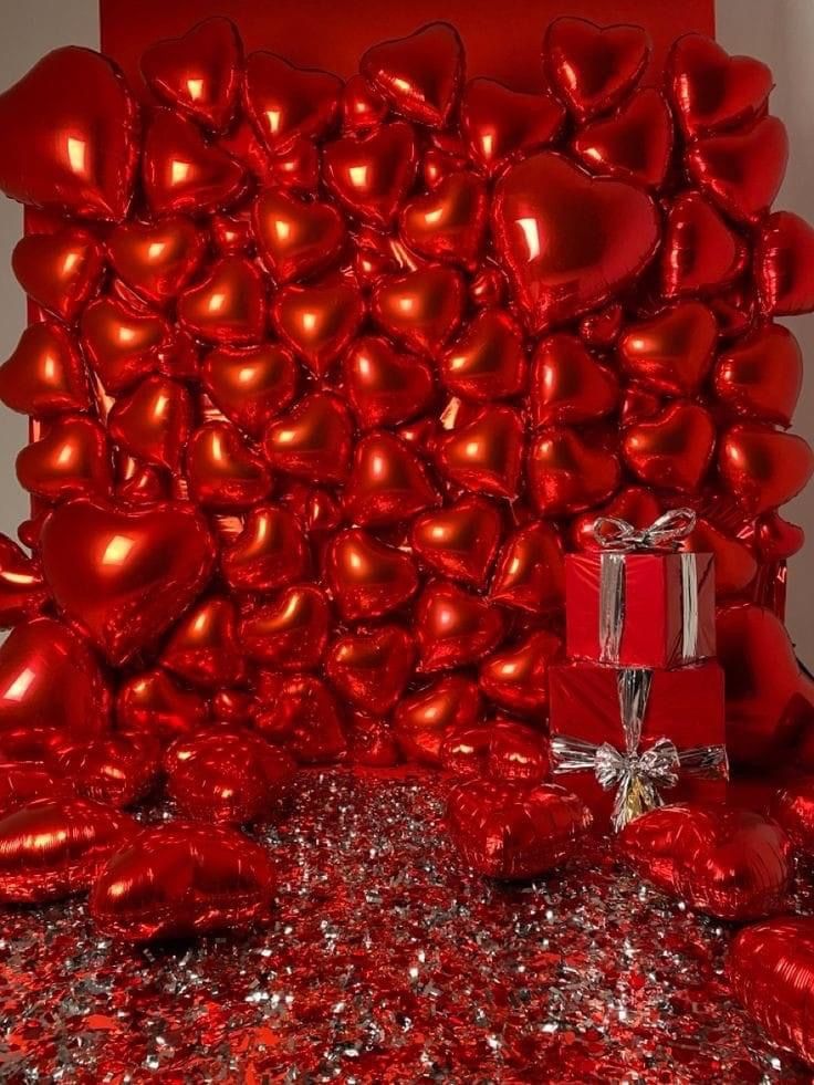 red heart balloons are arranged on the floor next to a gift box and wrapped in silver foil