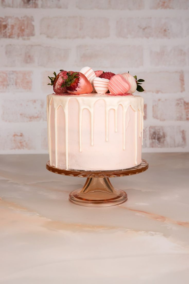 a white cake topped with strawberries on top of a wooden table next to a brick wall