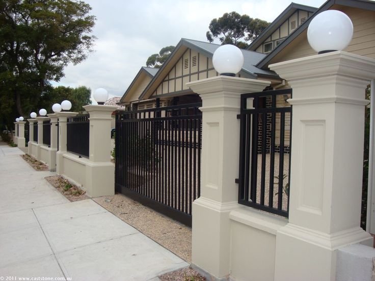 a white fence with black iron gates and lights on it's posts in front of a house