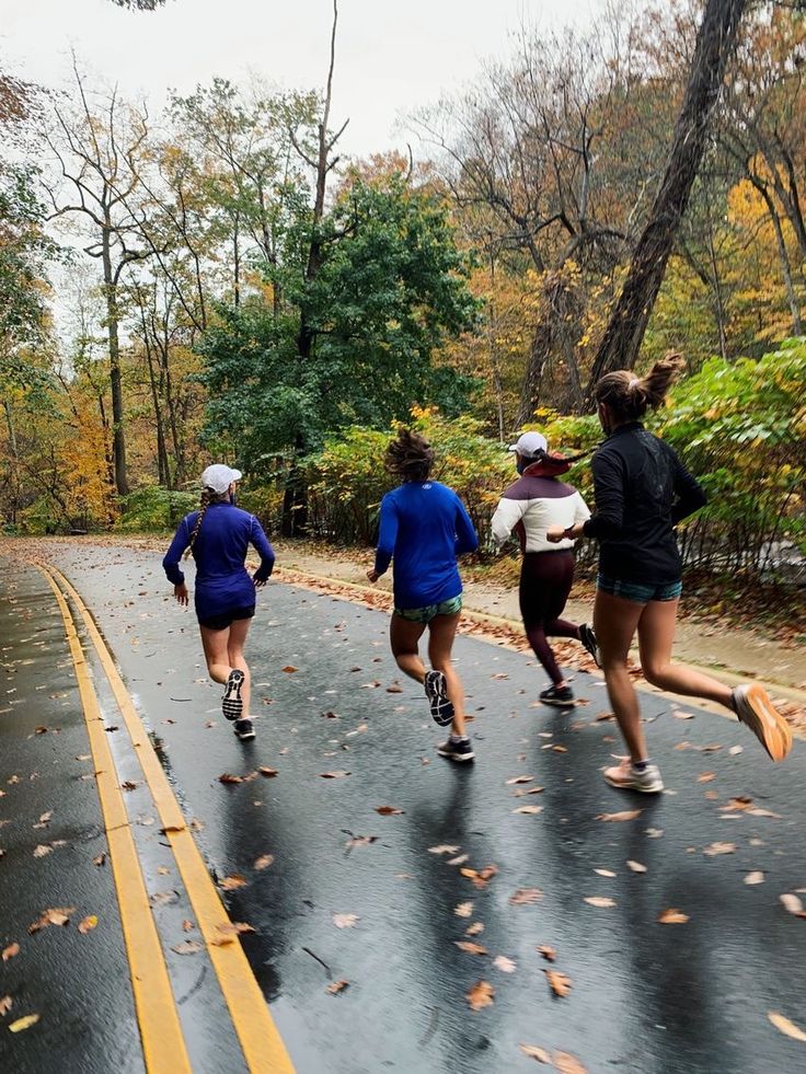 four people running down the road on a rainy day with trees and leaves in the background