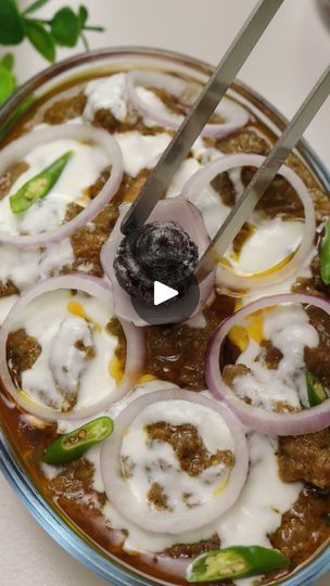 a bowl filled with meat and onions on top of a white table next to a knife