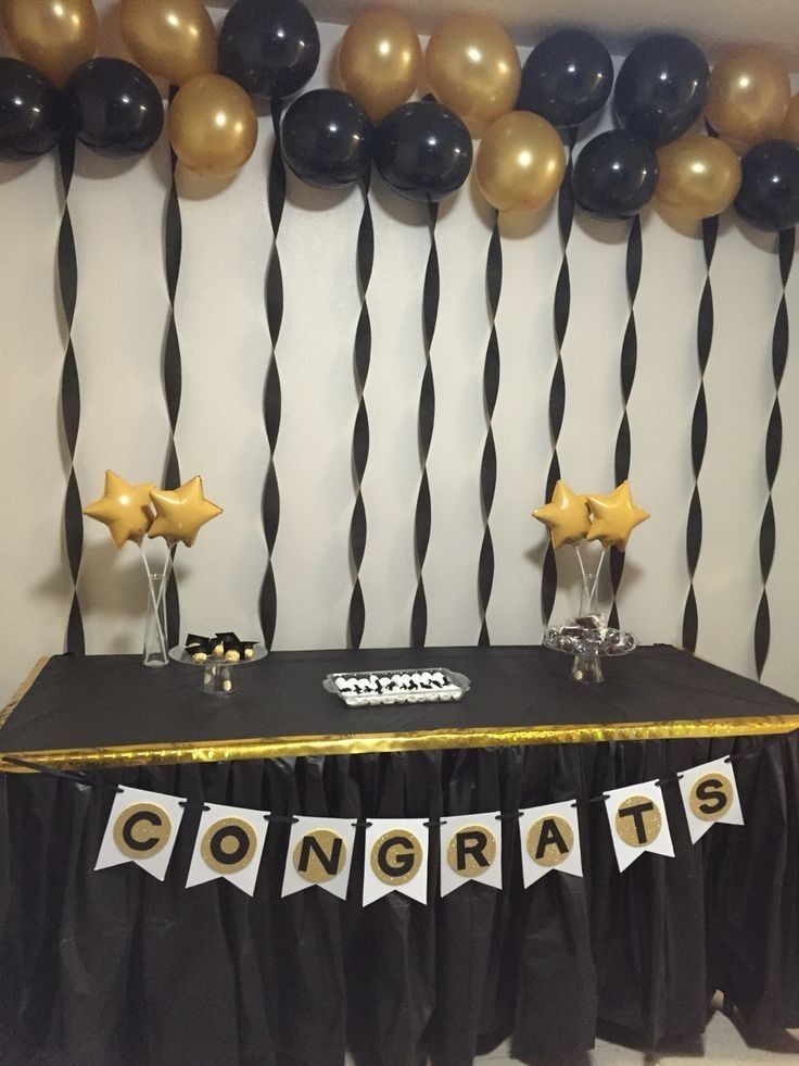 a table with black and gold decorations on it in front of a balloon wall that says congrats