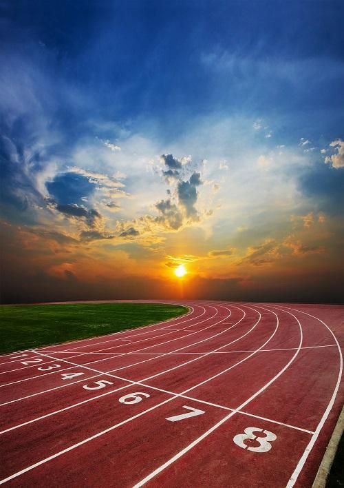 a running track with the sun setting in the background and clouds above it, as seen from behind