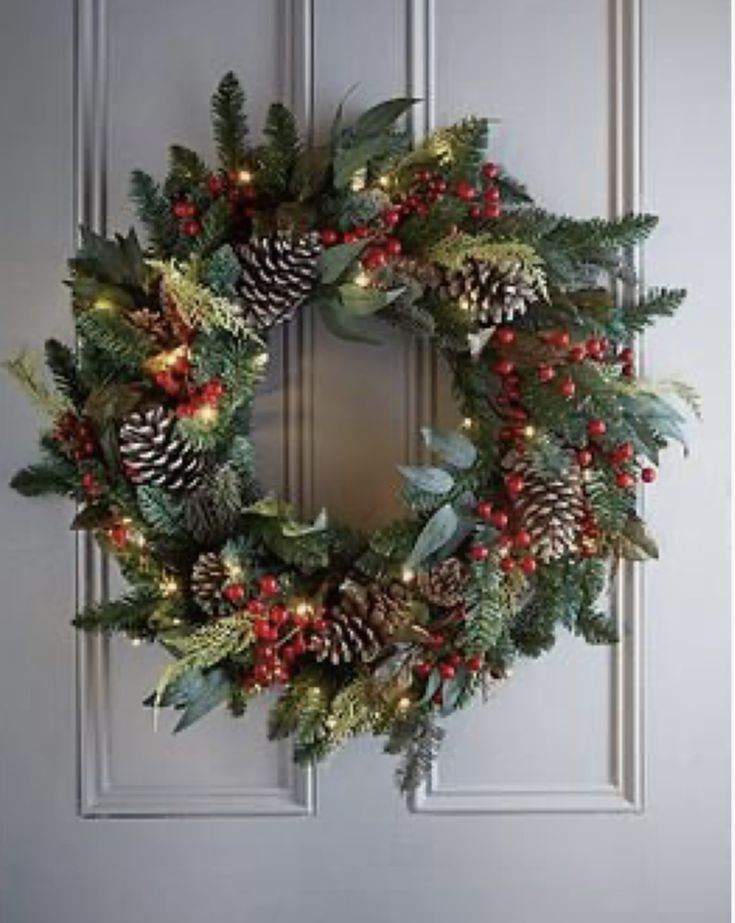 a christmas wreath with pine cones and red berries on the front door, lit by lights