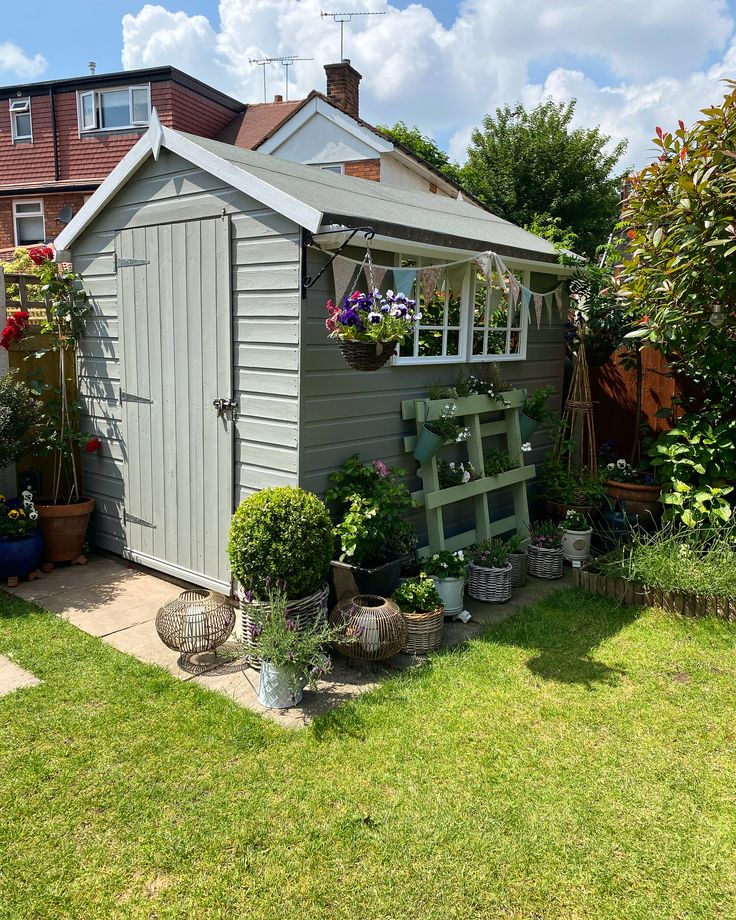 a garden shed with potted plants and flowers in the back yard, on a sunny day