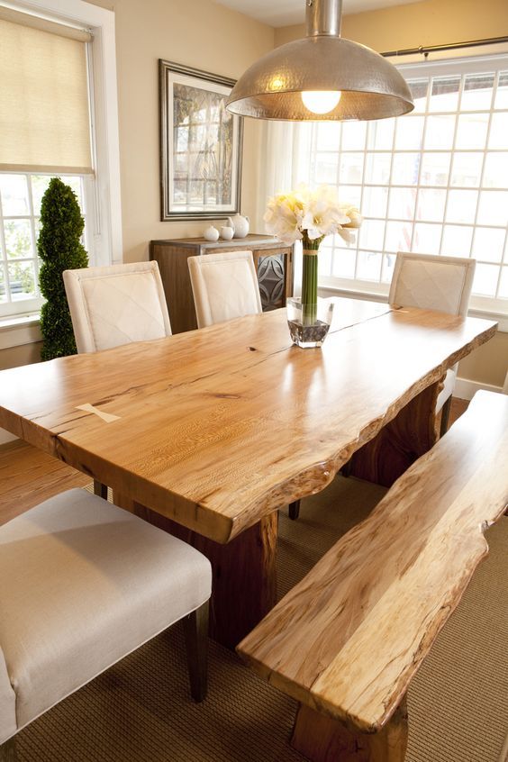 a large wooden table with white chairs and a bench in front of it, next to a window