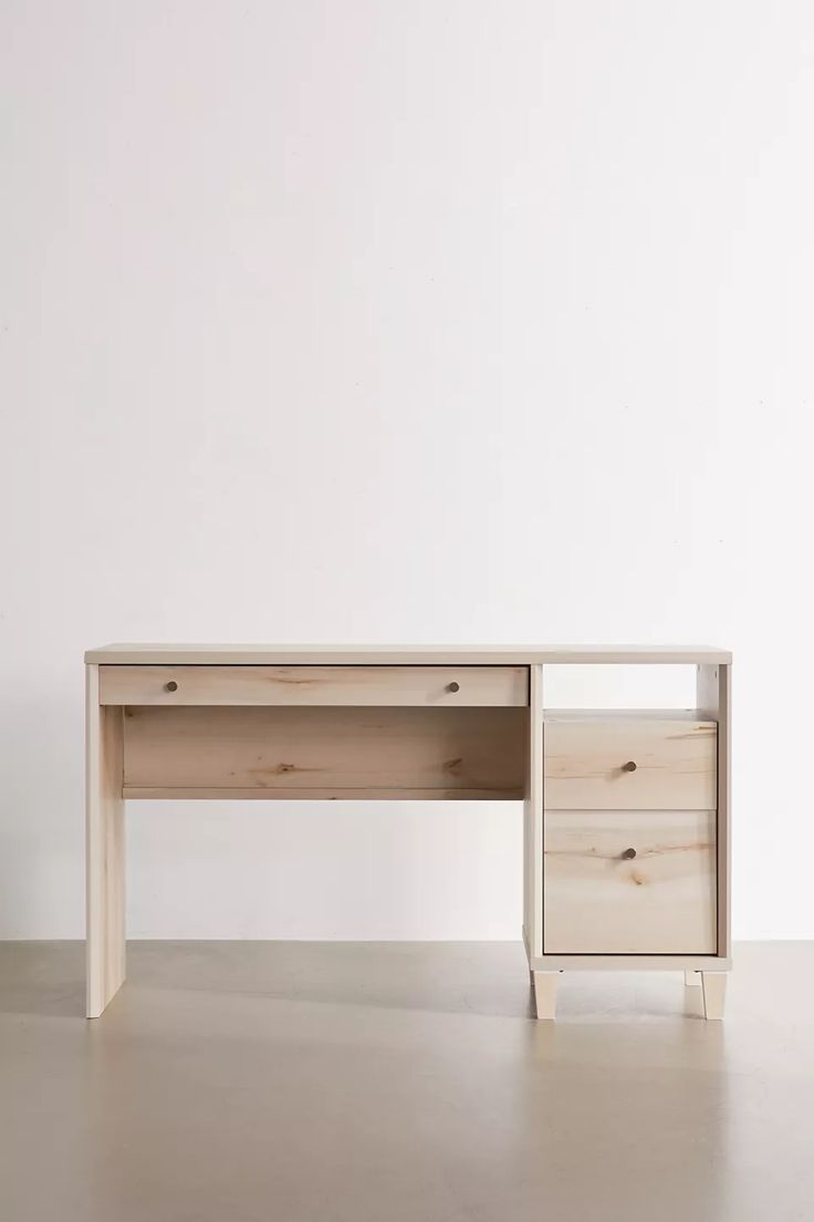 a white desk with two drawers sitting on the floor next to a plant in a vase