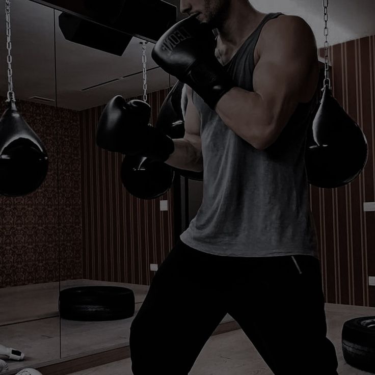 a man wearing black boxing gloves in a gym with two punching mitts hanging from the ceiling