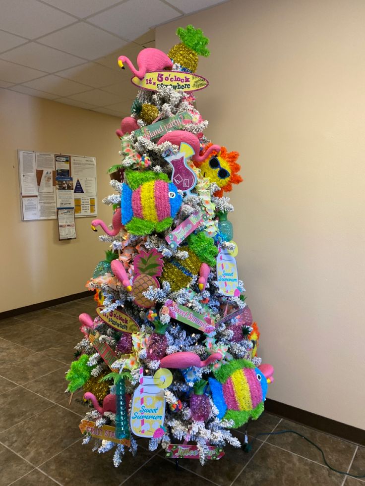 a brightly colored christmas tree in the corner of an office building with decorations on it