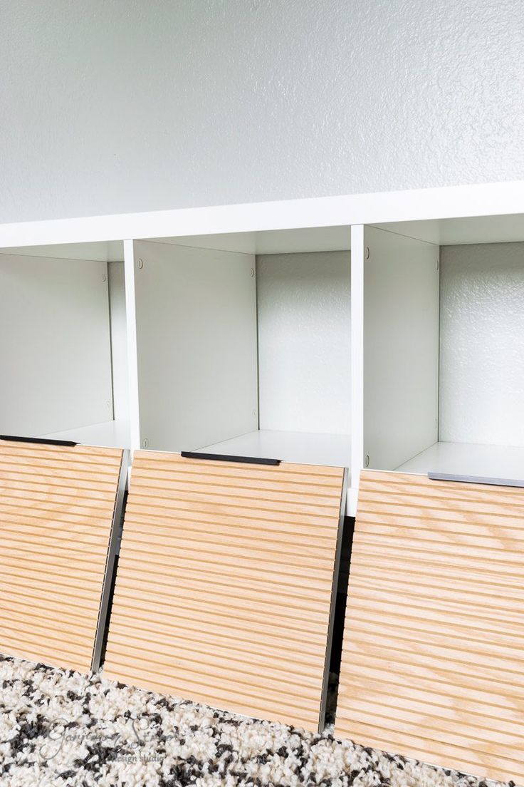 three white shelves with wooden slats on them in a room that has carpeted flooring