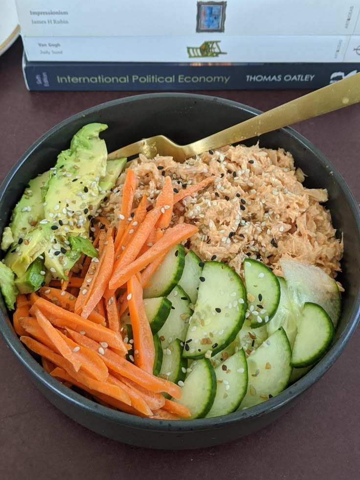 a bowl filled with carrots, cucumbers and other vegetables next to a book