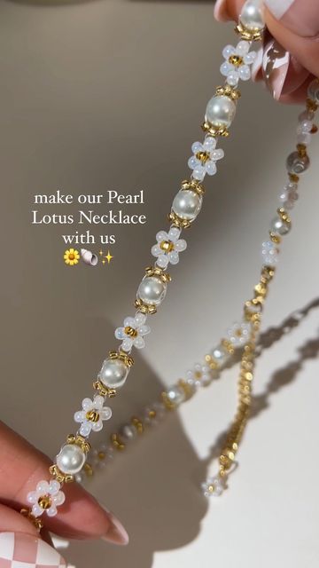 a close up of a person's hand holding a necklace with pearls and flowers on it