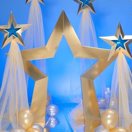 three gold stars and two white balloons in front of blue backdrop with sheer netting over them