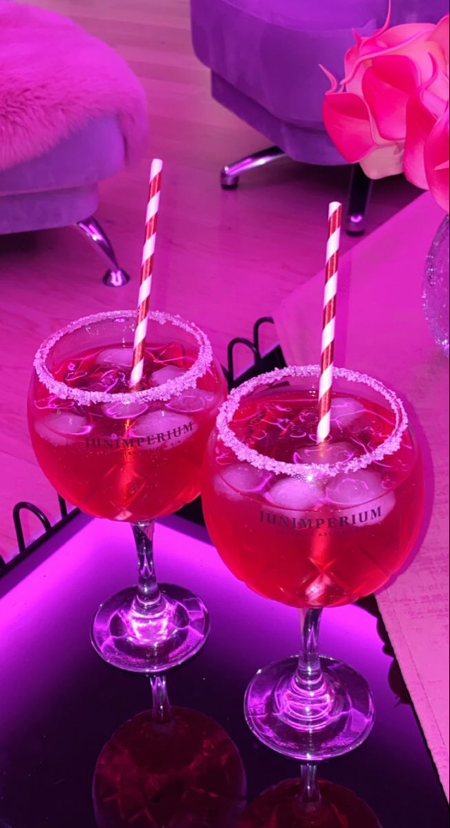 two glasses with drinks sitting on top of a purple table next to a pink rose