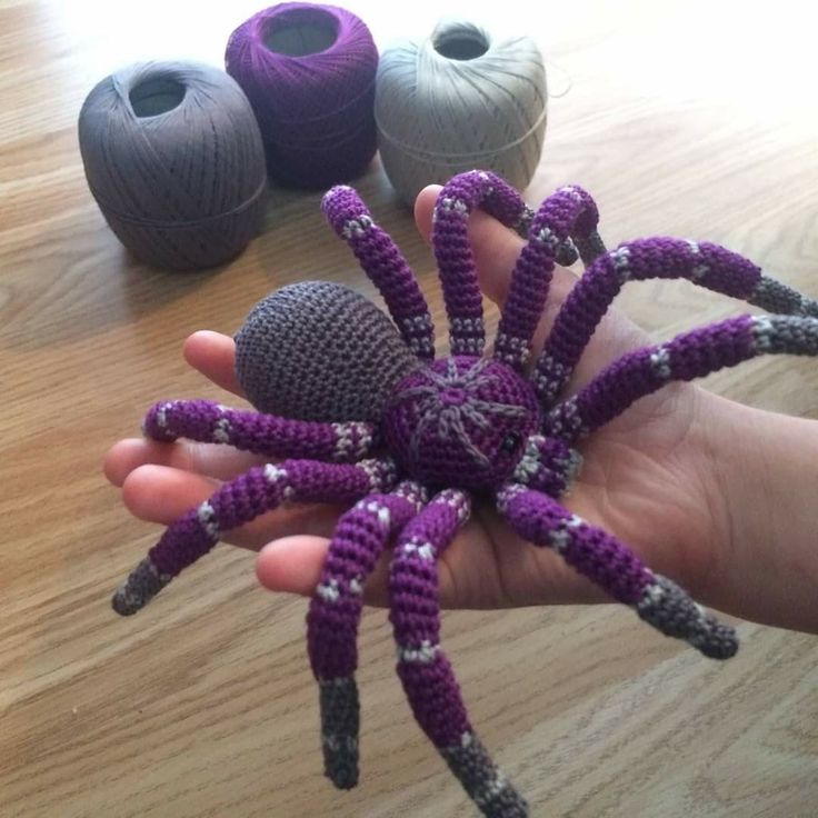 a hand holding a purple crocheted spider next to two balls of yarn