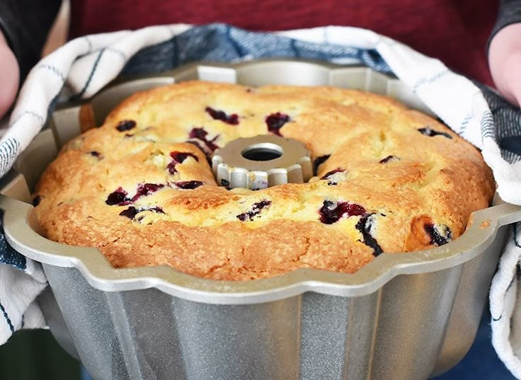 a person holding a cake pan with blueberries in it and a pie crust on the bottom