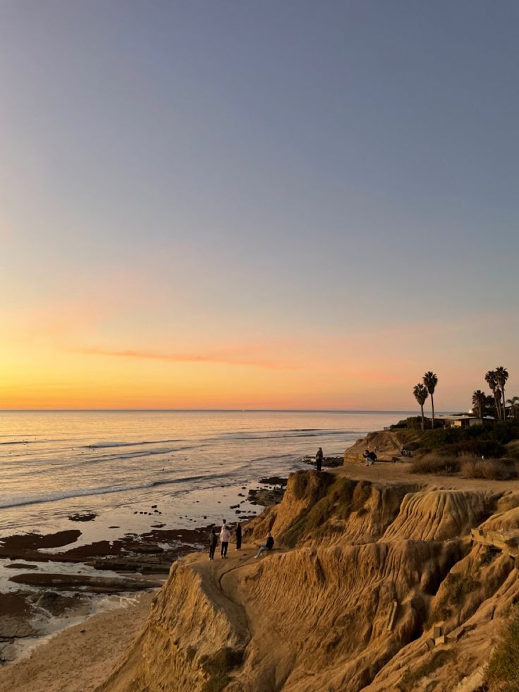 people are walking along the beach at sunset