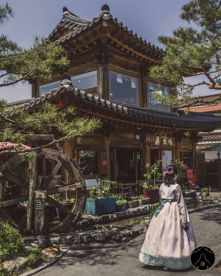 a woman in traditional japanese dress standing near a building with a water wheel on the street