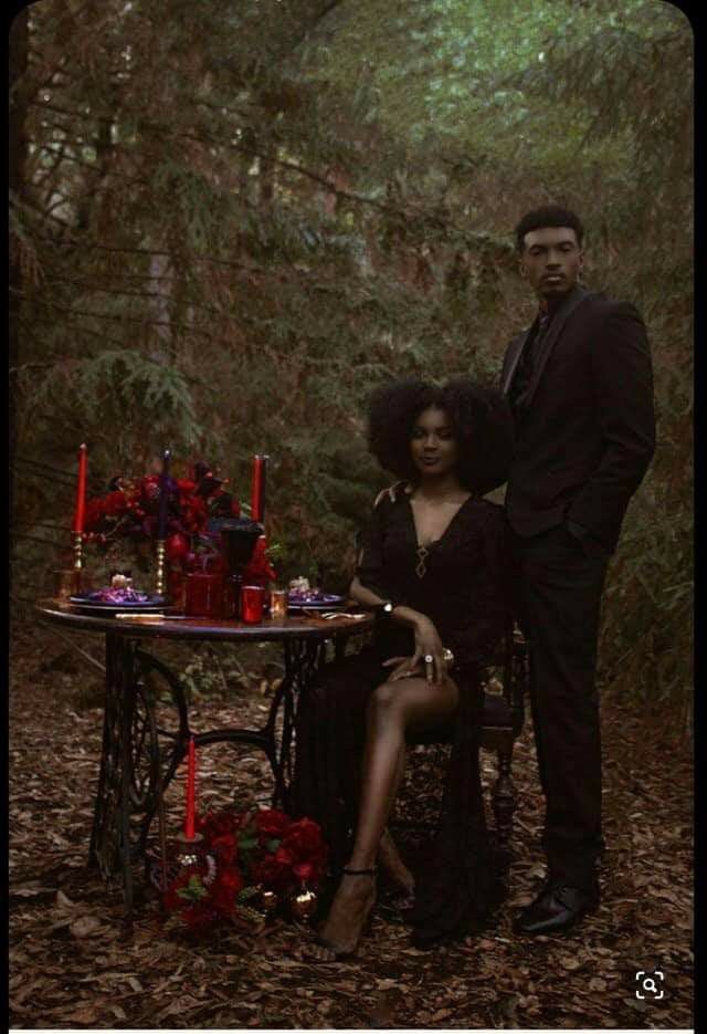 a man and woman are sitting at a table in the woods with candles on it