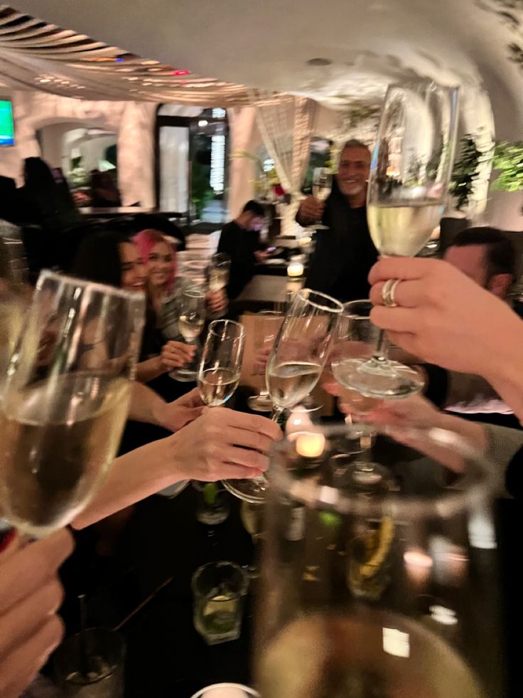 a group of people toasting with wine glasses on a table in a room full of people