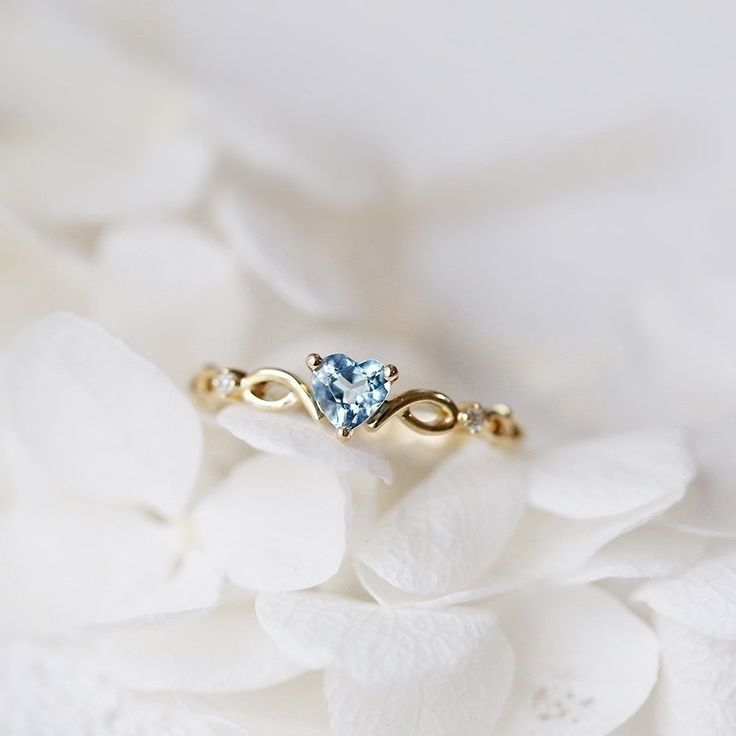 a gold ring with a blue topazte surrounded by white flowers on a bed of petals