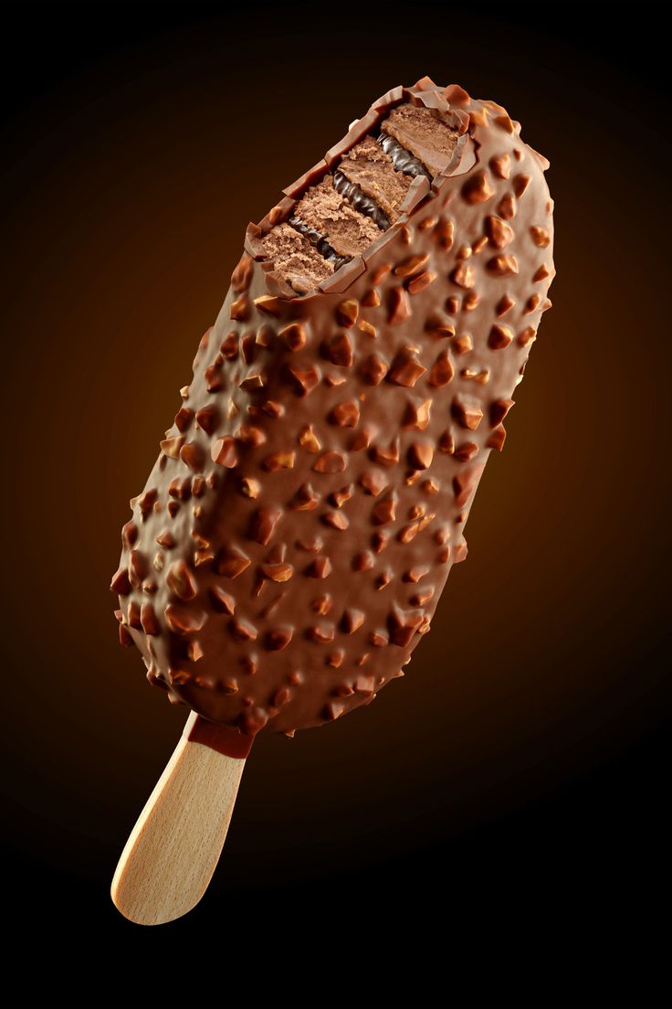 an ice cream with chocolate sprinkles on a wooden stick in front of a black background