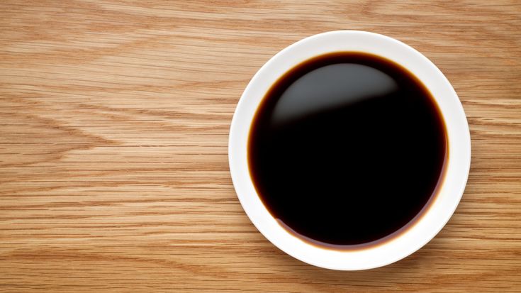 a cup of black coffee sitting on top of a wooden table next to a spoon