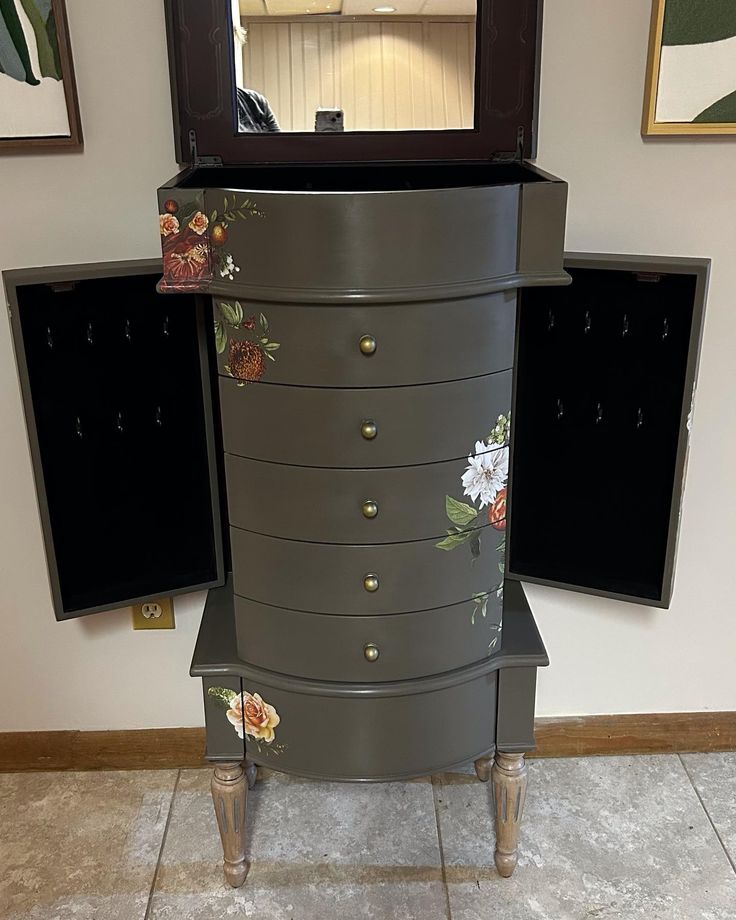 a dresser with flowers painted on it and a mirror in the corner next to it