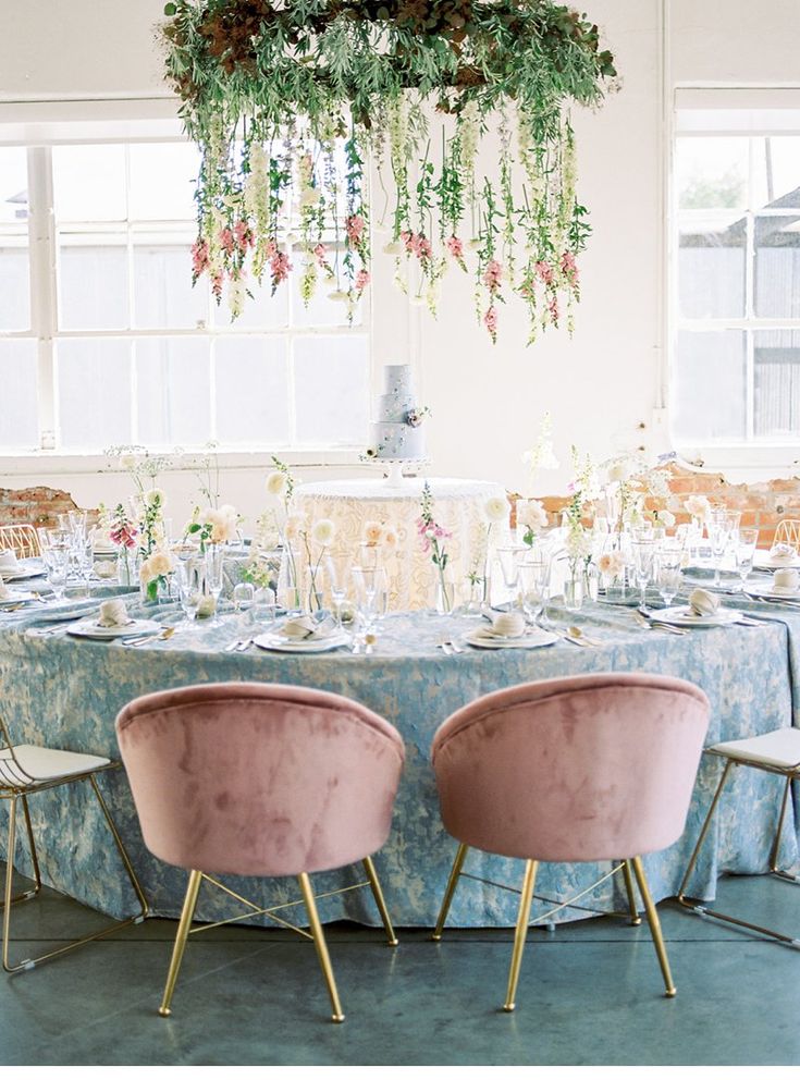 two pink chairs sitting at a round table with flowers hanging from it's ceiling