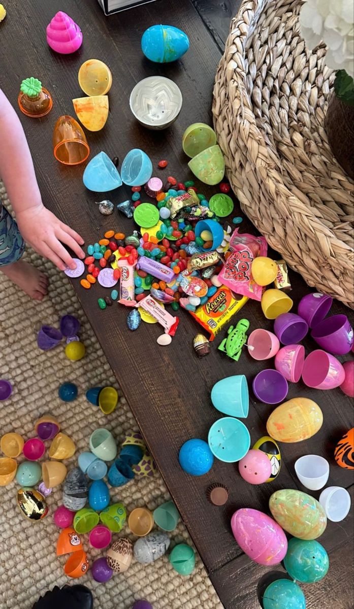 a child is playing with plastic eggs on the floor next to a basket full of candy