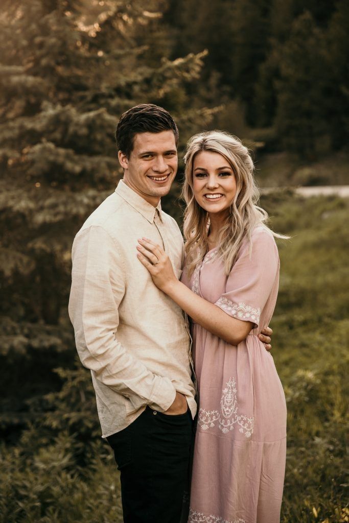 a man and woman standing next to each other in front of some trees with their arms around each other