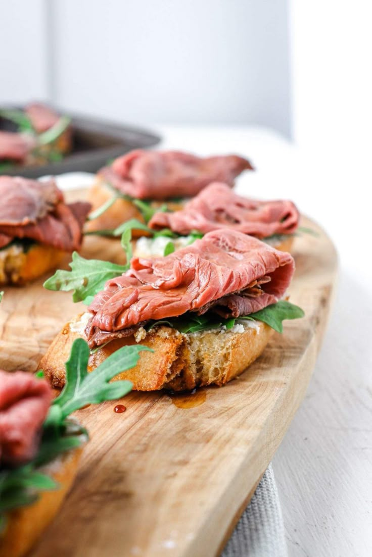 a wooden cutting board topped with sandwiches covered in meat and veggie toppings