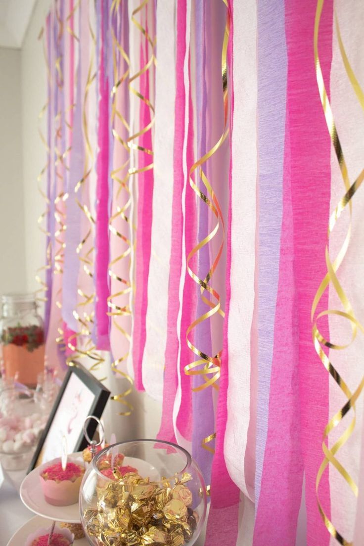 pink and gold streamers are hanging from the wall above a bowl of candy on a table