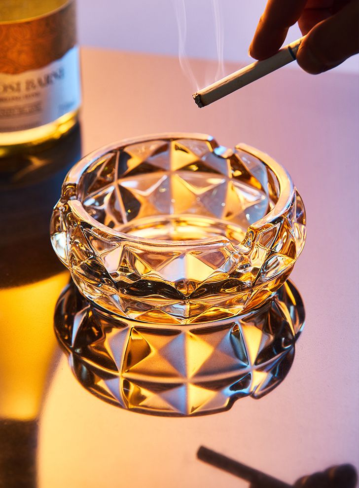 a glass ashtray sitting on top of a table next to a bottle