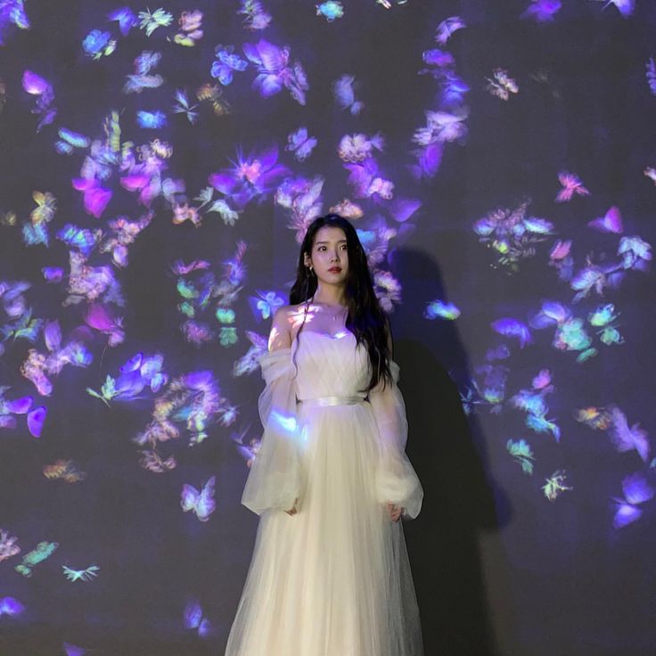 a woman standing in front of a wall with butterflies on it and wearing a white dress