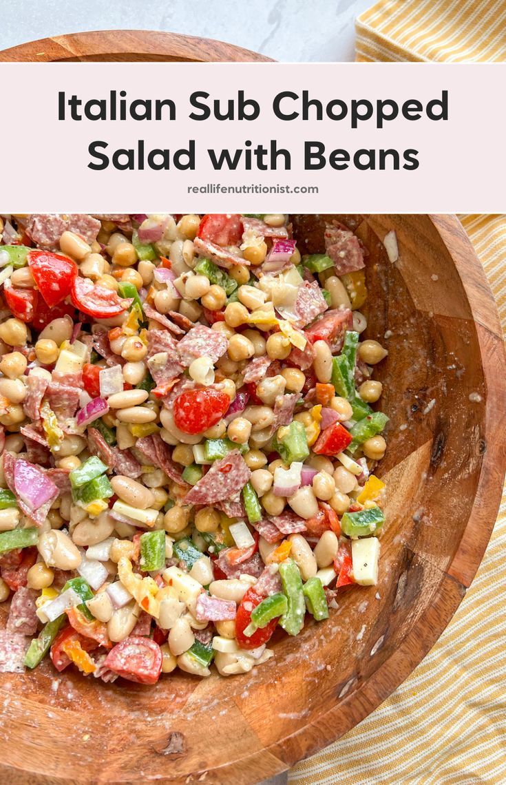 a wooden bowl filled with salad and beans on top of a striped table cloth next to a