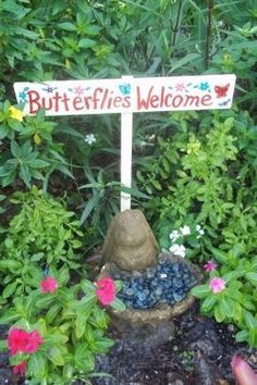 a sign that says butterflies welcome in front of some bushes and flowers with pink, red, purple, and blue flowers around it