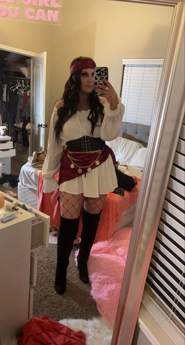 a woman taking a selfie in a mirror wearing a pirate costume and fishnet stockings