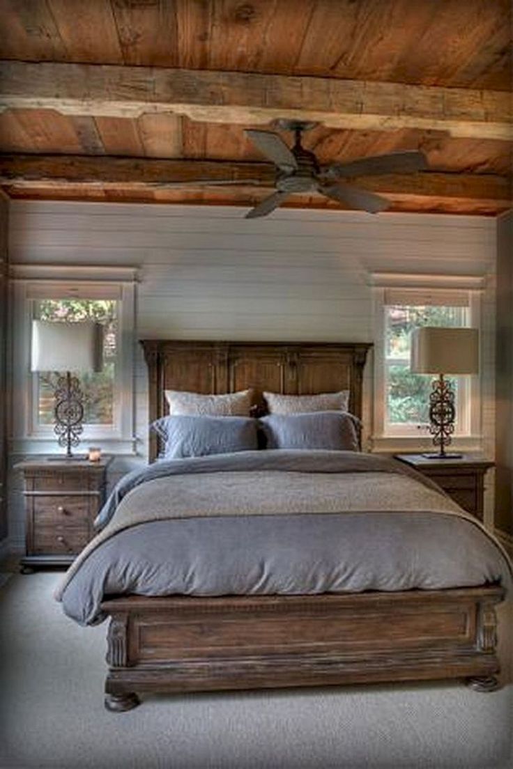 a large bed sitting under a ceiling fan in a bedroom next to two windows with wooden beams