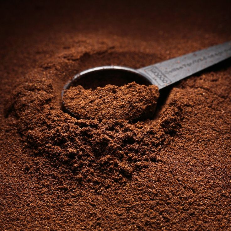 a scoop of cocoa powder with a measuring spoon in the middle on a brown background