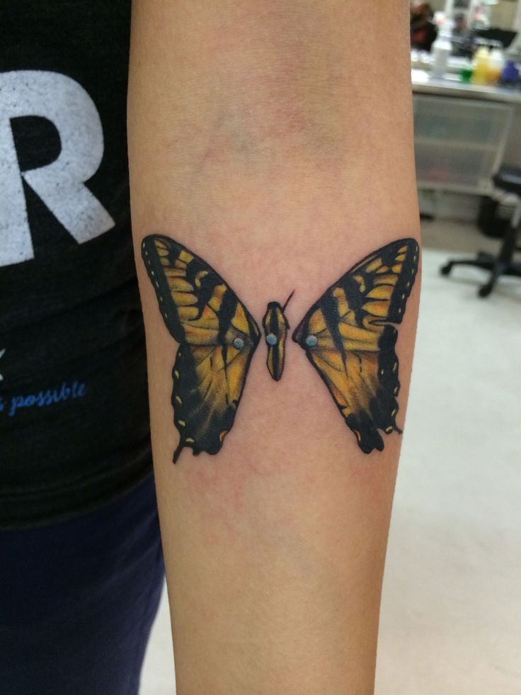 a woman's arm with a yellow and black butterfly tattoo on the left forearm