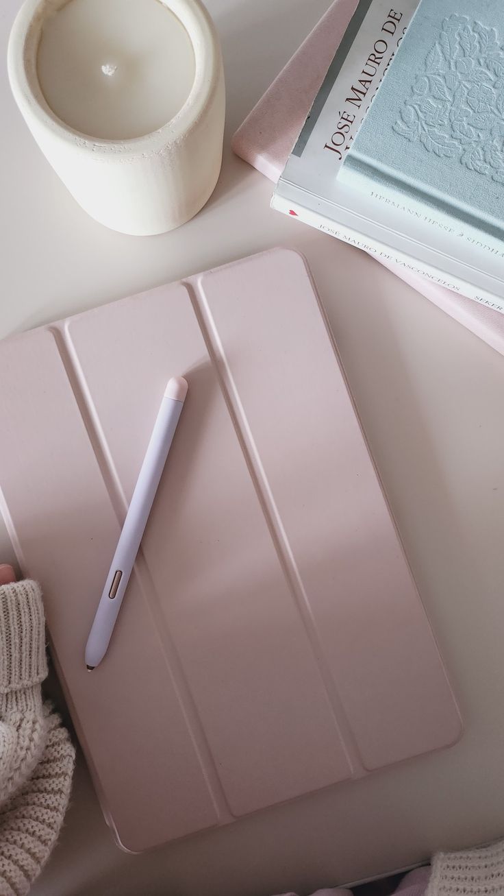 a pink notebook with a pen on top of it next to a white cup and saucer