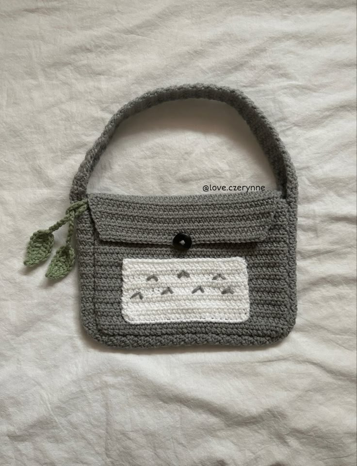 a crocheted purse with a green leaf on the front and two small buttons in the back