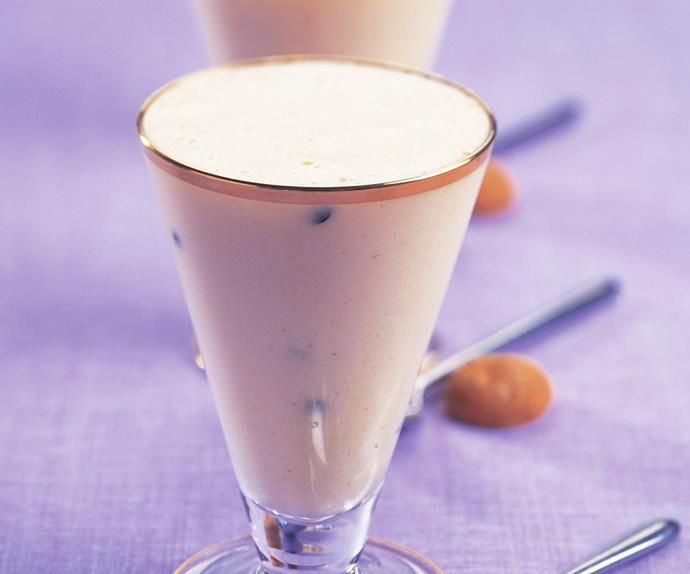 two glasses filled with milkshakes sitting on top of a purple cloth next to oranges