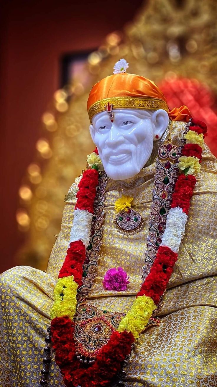 the statue is decorated with flowers and garlands on it's head, sitting in front of a gold background